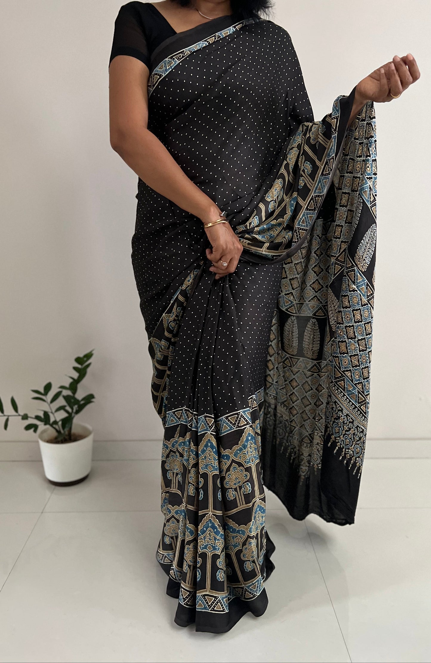 Woman wearing a black saree with a geometric pattern, holding it in front of a white background.