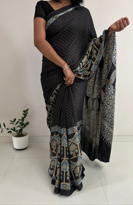 Woman wearing a black saree with a geometric pattern, holding it in front of a white background.